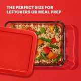 Glass food container with lid filled with rice and vegetables on a red background