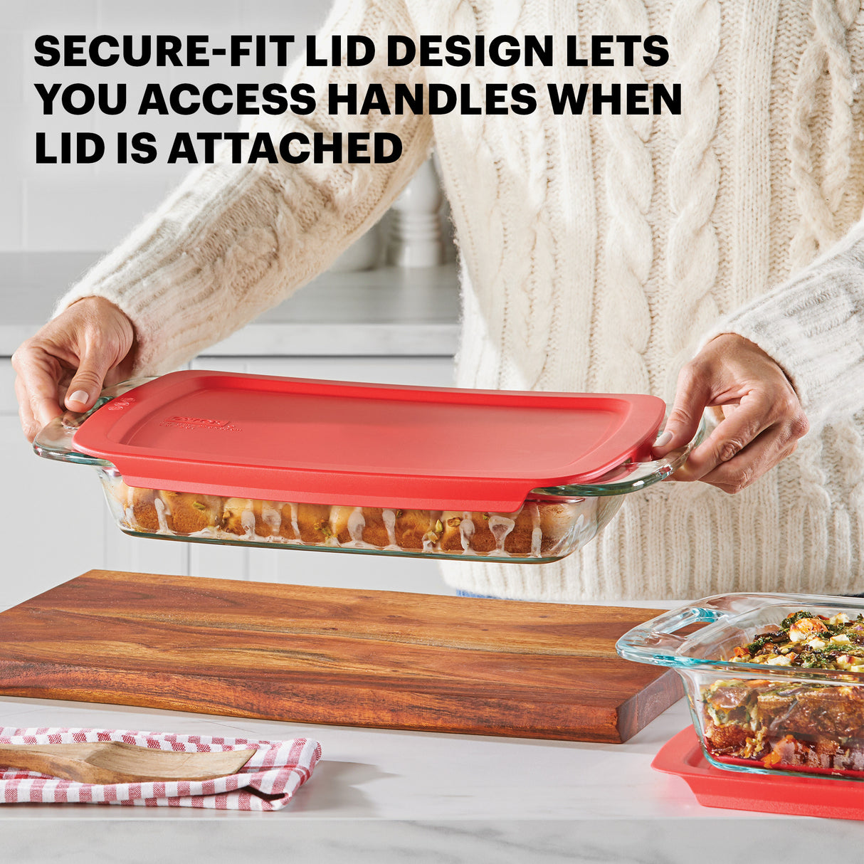 Person holding a glass dish with a red lid, demonstrating its secure-fit design.