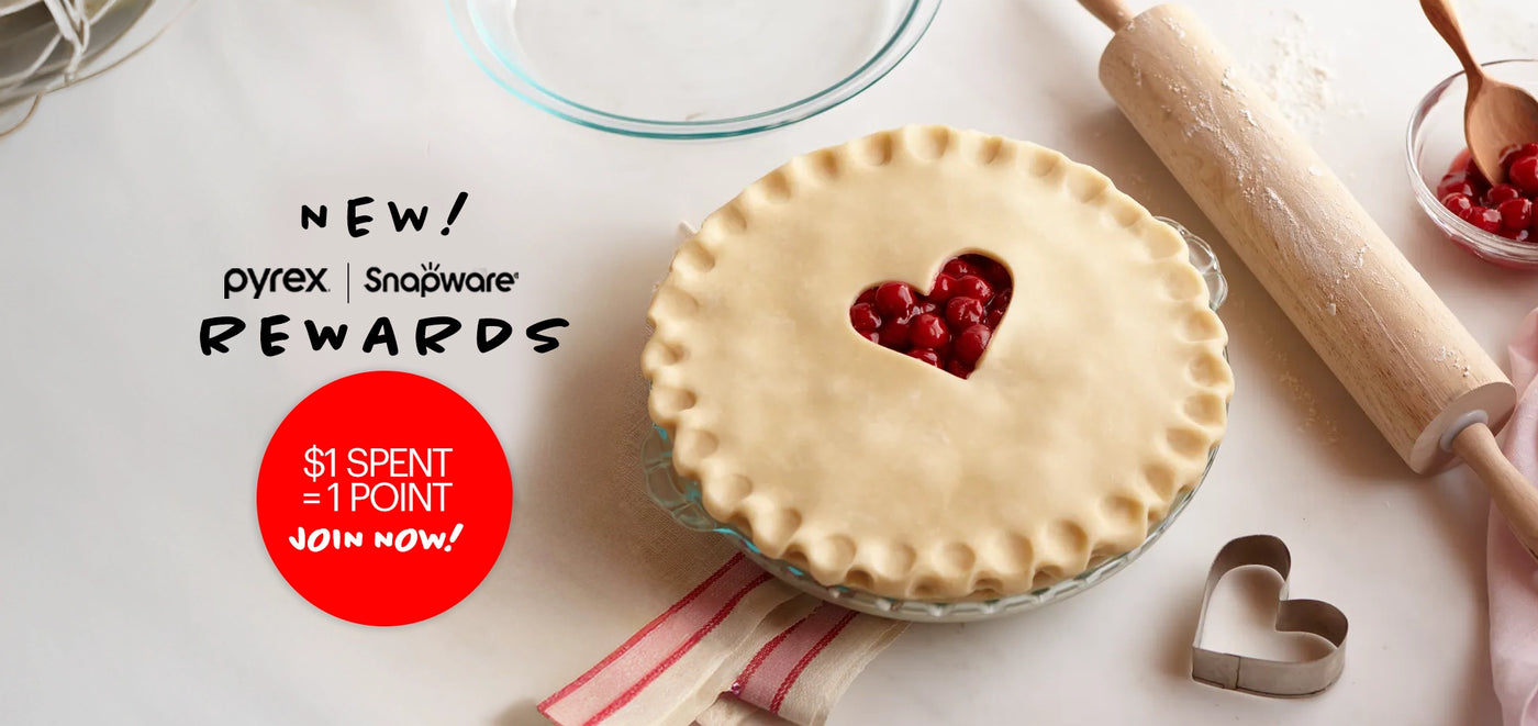 Pie with a heart-shaped cutout on top, rolling pin, and cherry pie filling on a white surface with 'pyrex' branding.