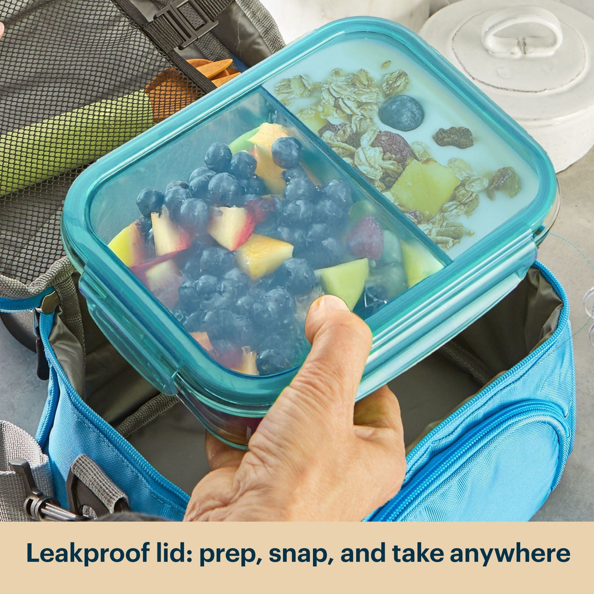 Hand holding a blue bento box with food inside, placed on a gray surface.