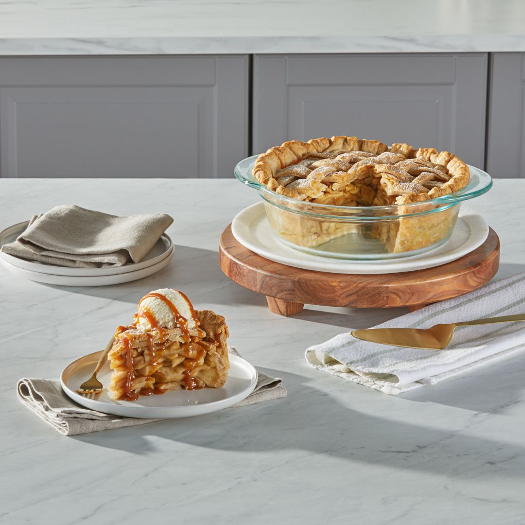 Apple pie with a slice served on a plate with ice cream, placed on a marble countertop.