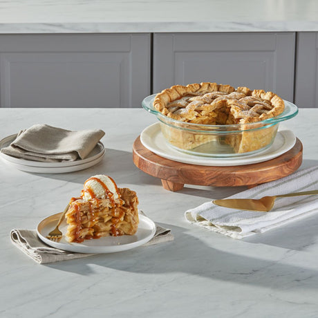 Apple pie with a slice served on a plate with ice cream, placed on a marble countertop.