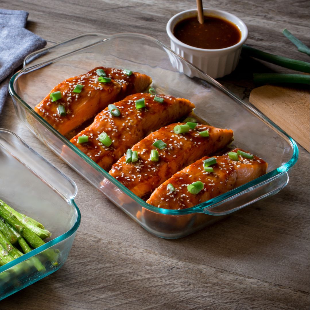 Glass dish with salmon fillets garnished with green onions on a wooden table.