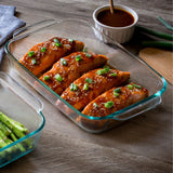 Glass dish with salmon fillets garnished with green onions on a wooden table.