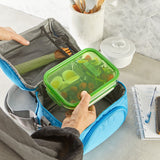 Person placing a green food container into a blue bag on a kitchen counter.