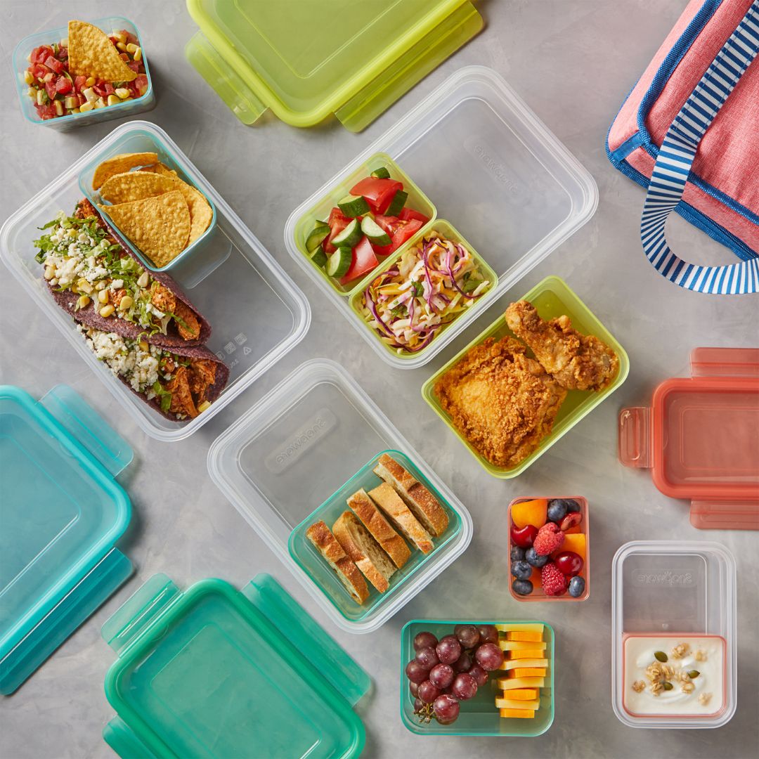 Assorted lunch containers with different food items on a gray surface