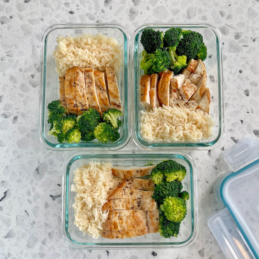 Three glass meal prep containers with chicken, rice, and broccoli on a gray surface.
