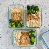 Three glass meal prep containers with chicken, rice, and broccoli on a gray surface.