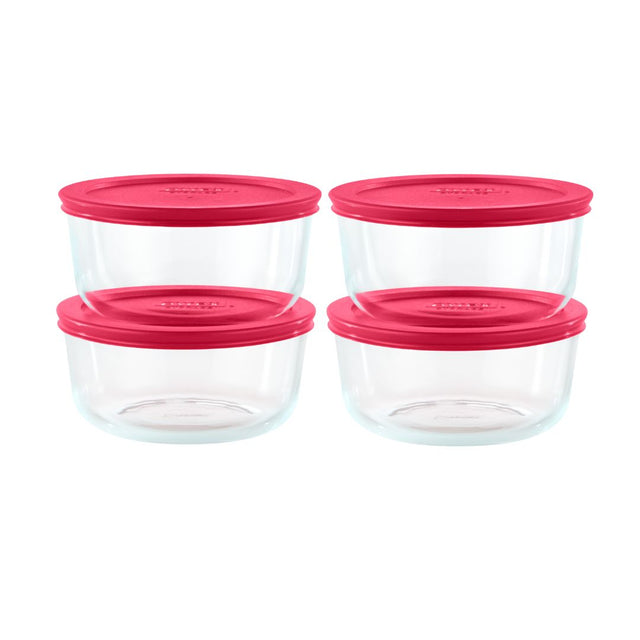 Set of four clear glass food storage containers with pink lids on a white background