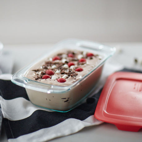 Glass container with dessert topped with berries and chocolate shavings on a striped cloth.