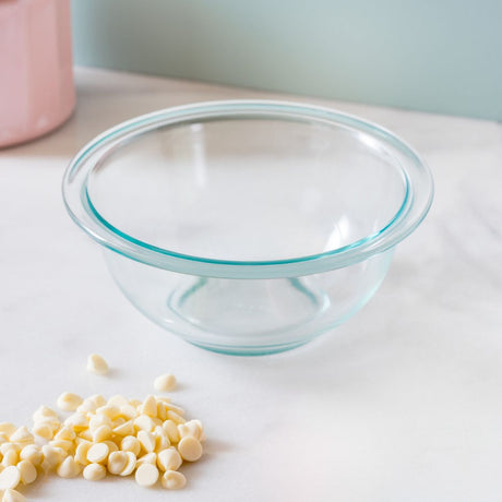 Clear glass bowl with blue rim on a white surface, surrounded by white chocolate chips.