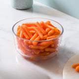 Clear glass bowl filled with orange carrot-like snacks on a light surface.