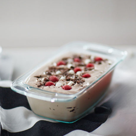 Frozen dessert with raspberries and chocolate shavings in a glass container on a striped fabric background