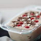 Ice cream with raspberries and chocolate shavings in a glass container.