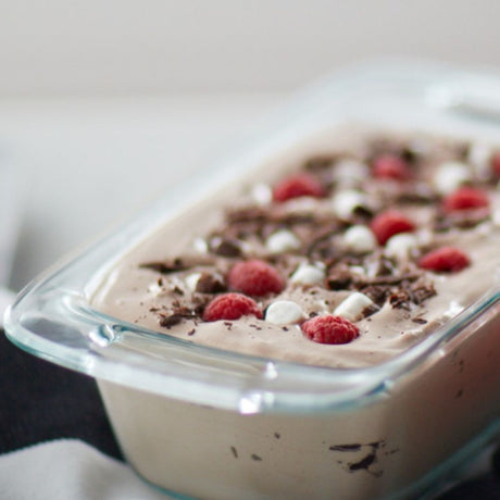 Ice cream with raspberries and chocolate shavings in a glass container.