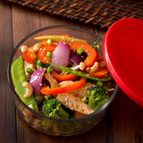 Glass container with a colorful vegetable salad and a red lid on a wooden surface