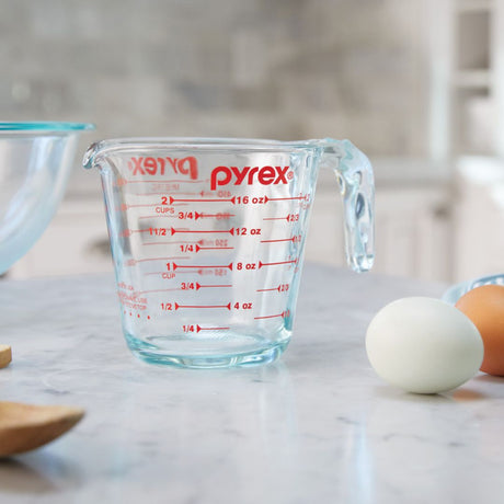 Pyrex measuring cup on a kitchen counter with eggs and a wooden spoon.