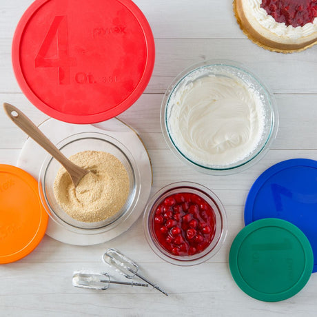 Bowls of ingredients with colorful lids on a white surface