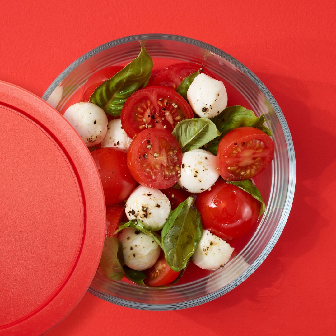 Caprese salad in a clear container with a red lid on a red background