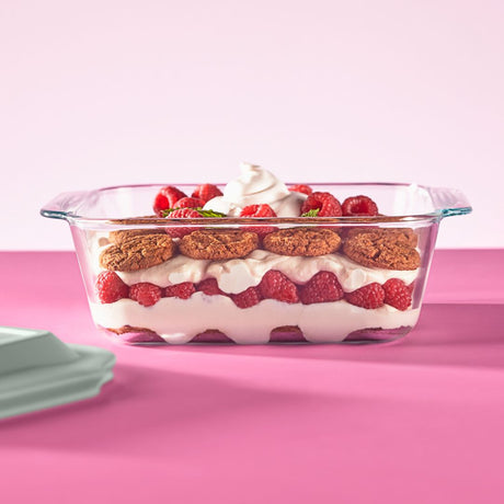 Glass dish with layered dessert including raspberries and cookies on a pink background