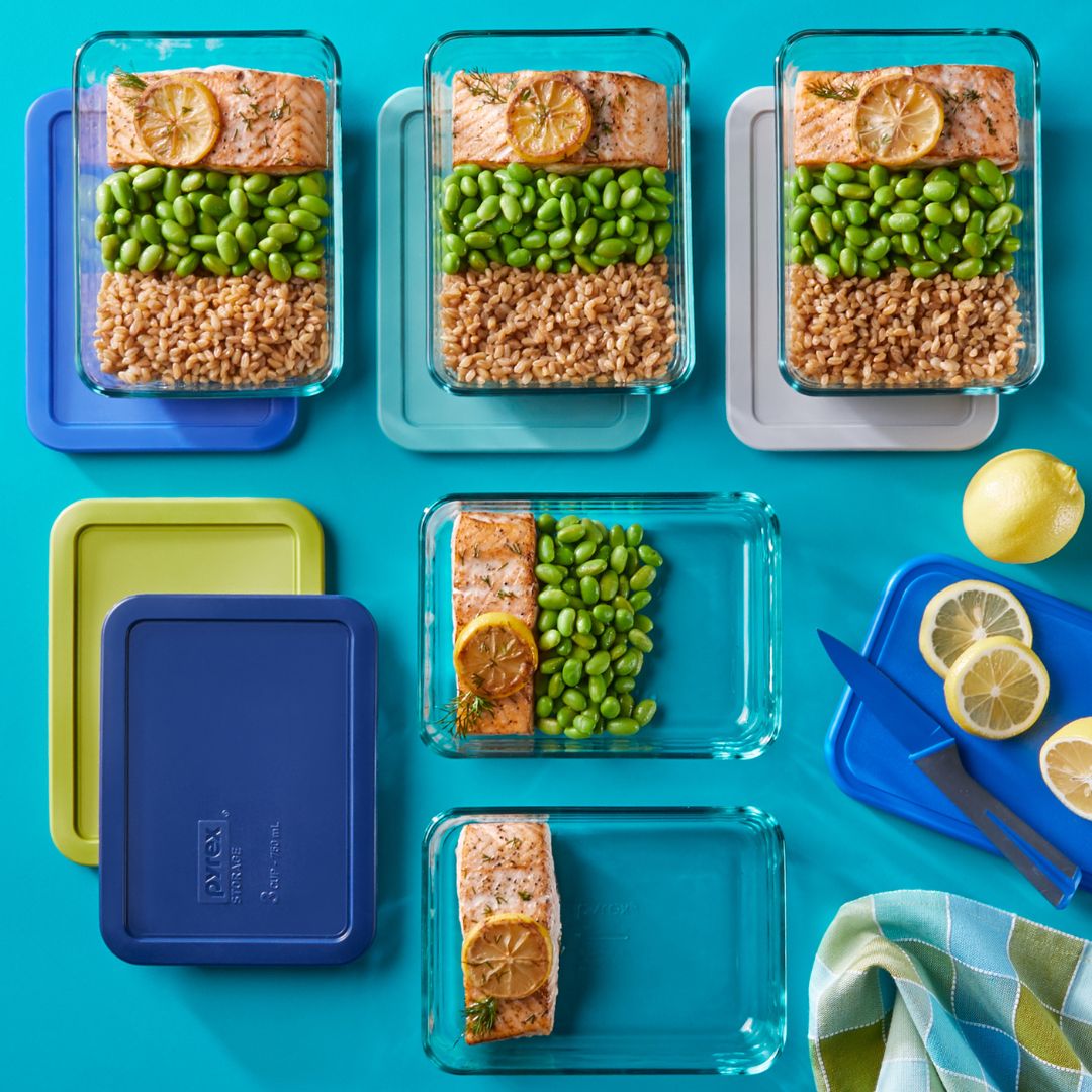 Multiple glass meal prep containers with food on a blue background