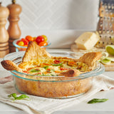 Golden-brown savory pie baked in a clear glass dish with melted cheese, cherry tomatoes, and herbs on top.