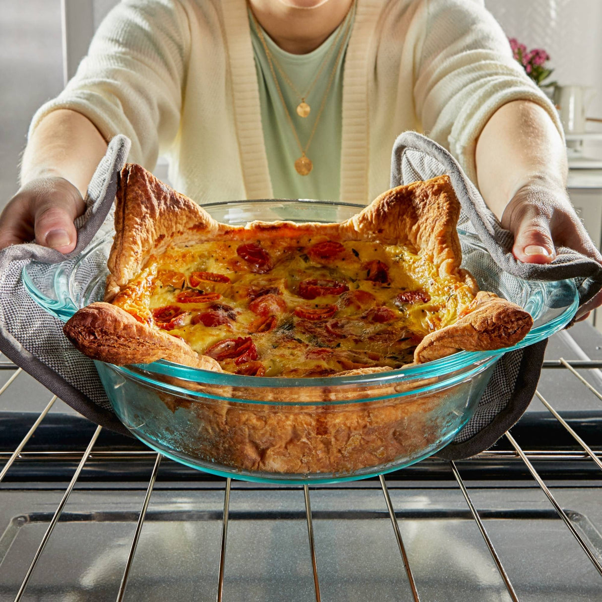 Person placing a freshly baked quiche in a clear glass dish onto an oven rack.