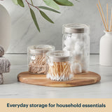 Clear jars with household essentials on a wooden tray with a neutral background