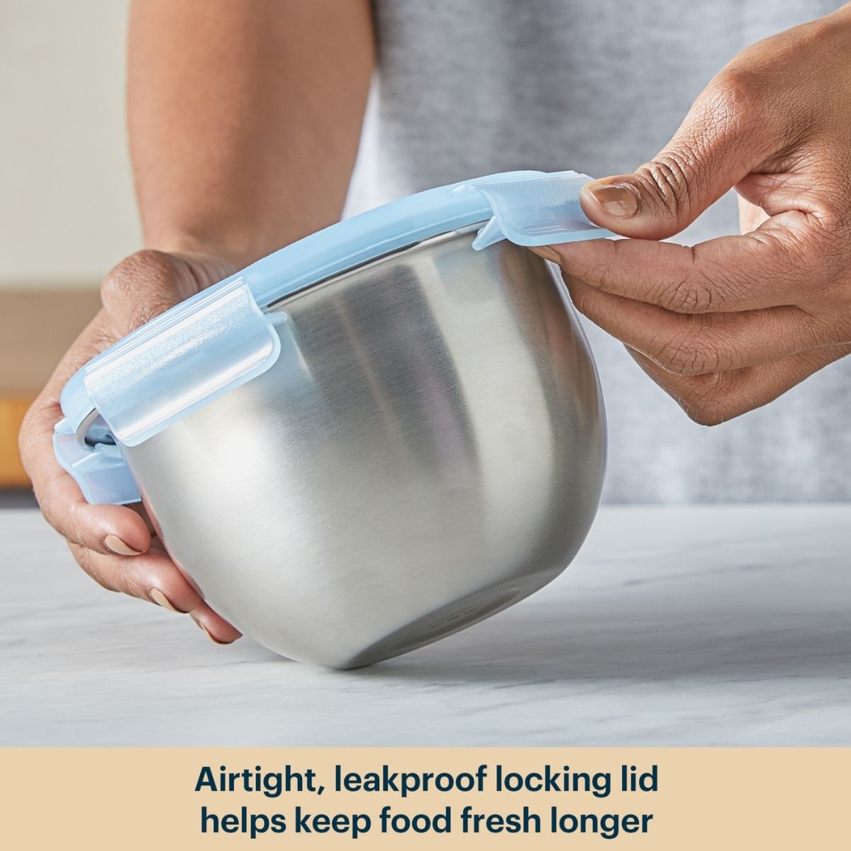 Person holding a stainless steel bowl with a blue airtight lid, emphasizing freshness.